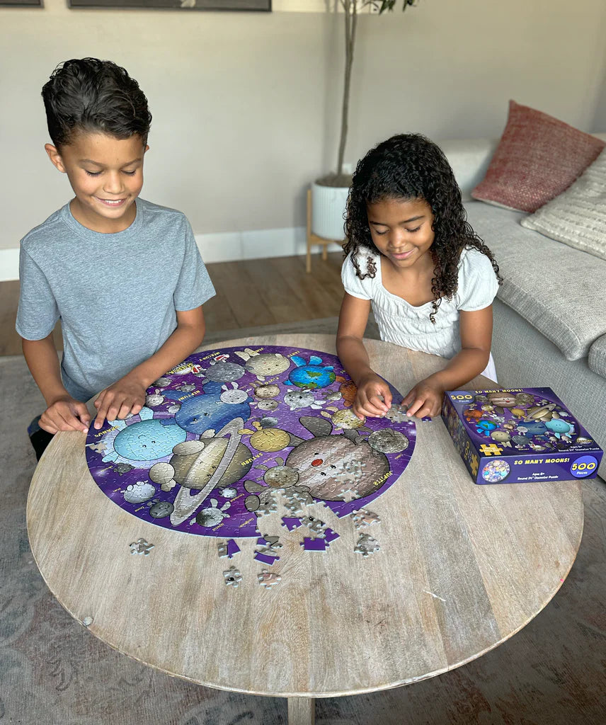 Two children working on a puzzle at a table with a completed puzzle and box in front of them.