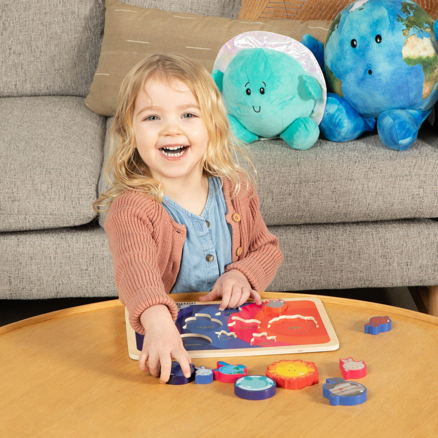 Child playing with a colorful puzzle on a wooden table, with plush toys in the background.